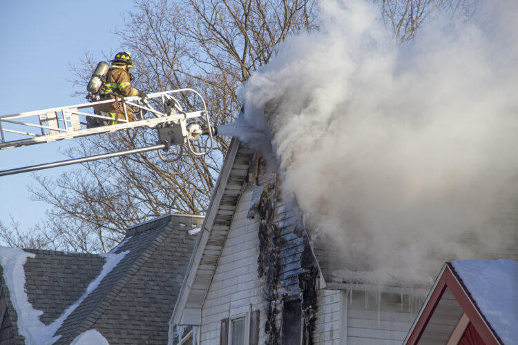 Escanaba Public Safety's Det. Lt. Tabitha Turnacliff is at the top of ladder truck 35 with a jet spraying the peak of a burning house.